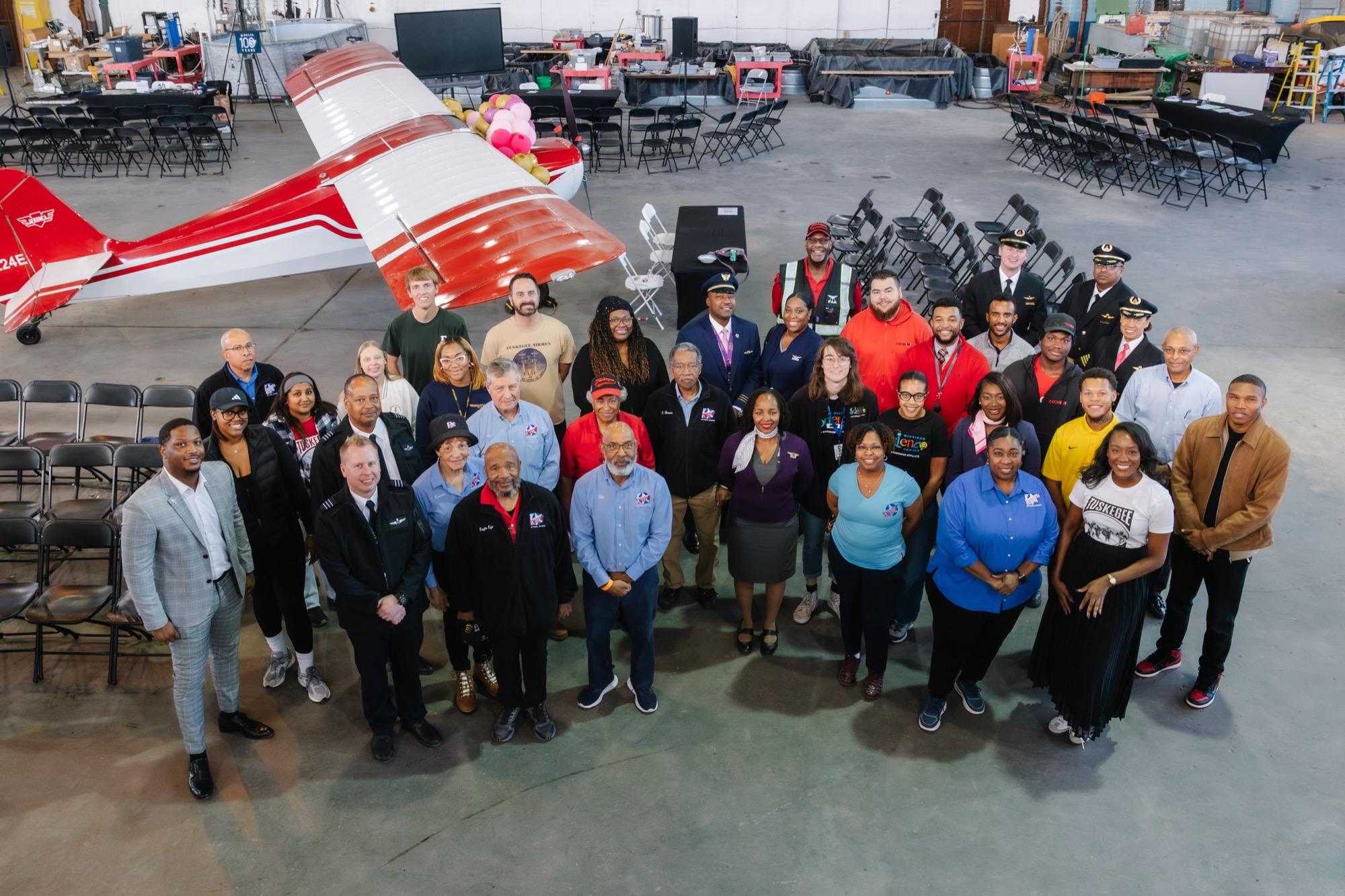 Large group of volunteers and staff gathered for an event with a vintage aircraft